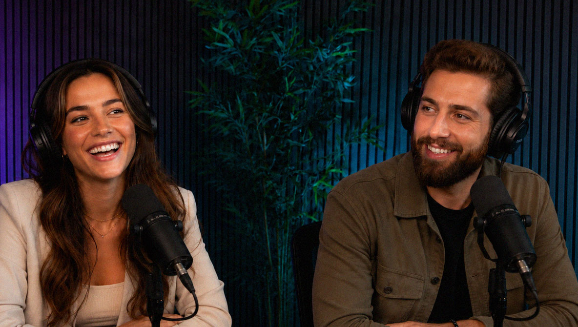 Two podcast hosts laughing behind microphones in the Pod Rush Studios recording room